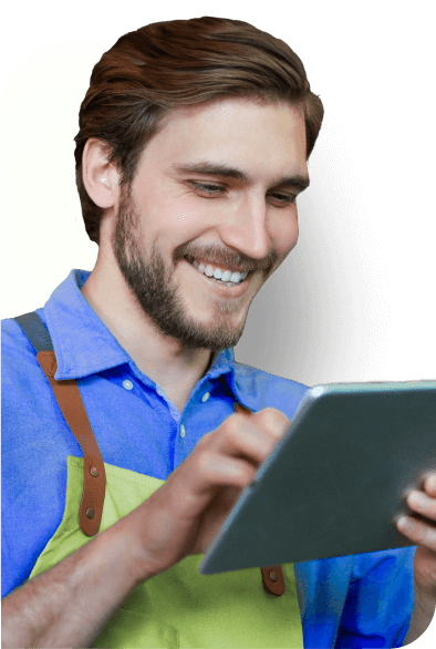 Homem sorrindo, olhando para o seu notebok. Camisa azul e macacão verde