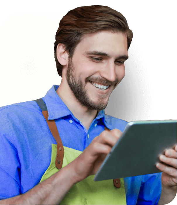 Homem sorrindo, olhando para o seu notebok. Camisa azul e macacão verde